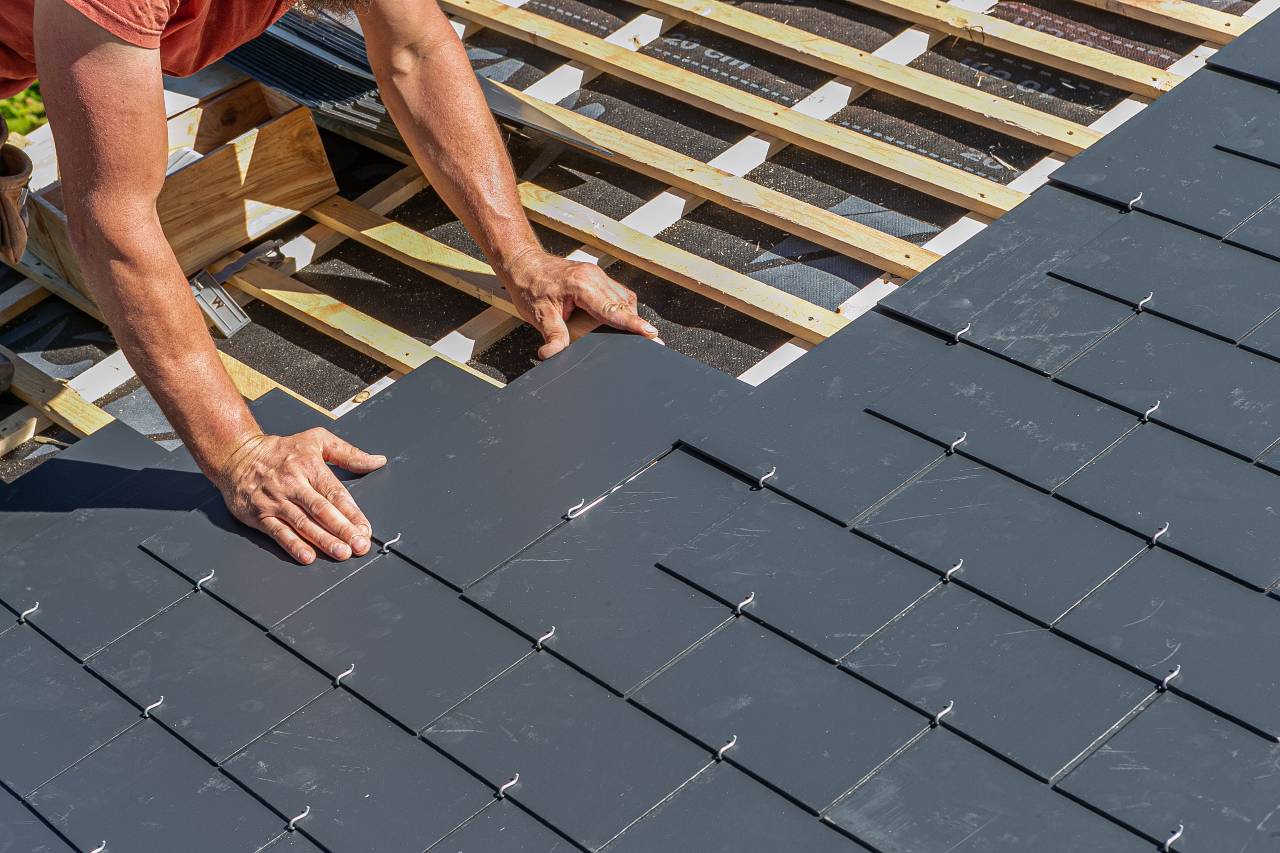 A professional roof installer laying slate tiles on a commercial roof.