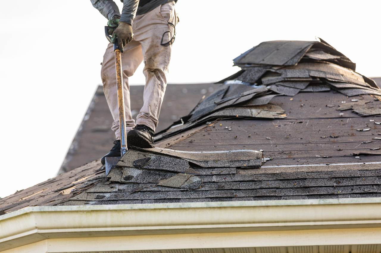 A roofing contractor removing shingles as part of a roof replacement project.